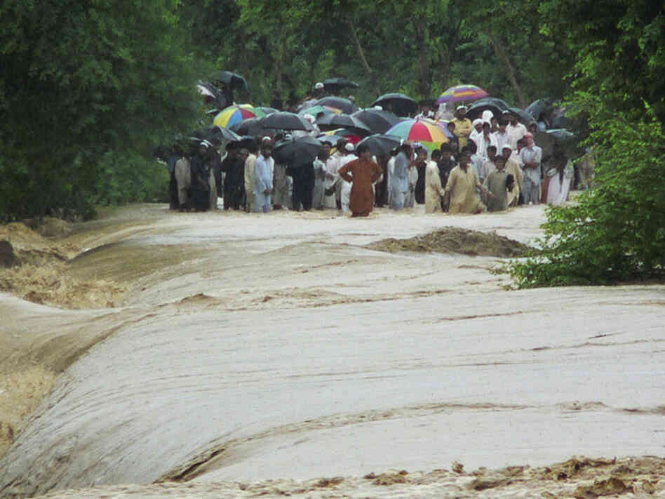 People wait to cross a flooded road in Bannu, Pakistan. People wait to cross a flooded road in Bannu, Pakistan.